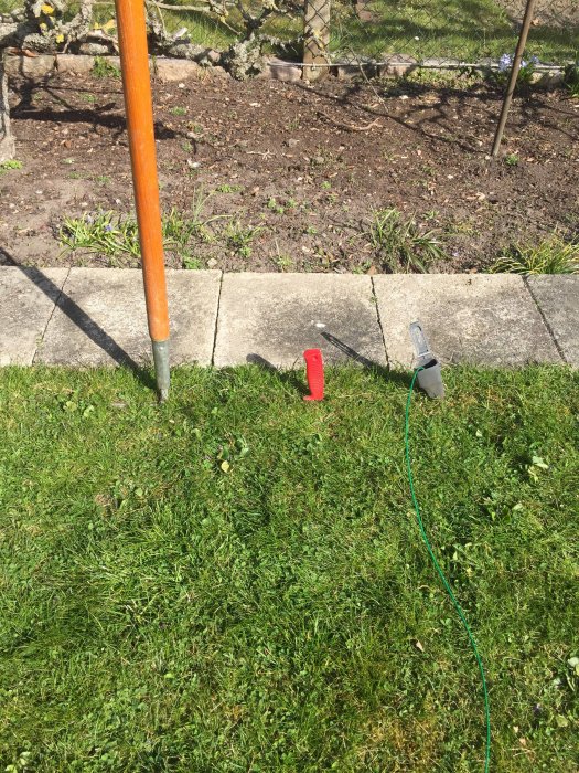 Kabel nedtryckt i gräsmattan med röd kantskärare och grön kabel synlig, omgiven av blommor och plattor.