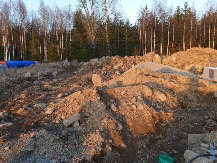 Hög med fyllnadsmassor och stenar från villa grundarbete i skogsmiljö, med stora stenar synliga.