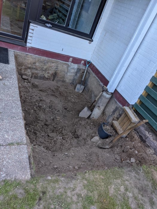 Uppgrävningsarbete för pool med spade, skottkärra och synlig husgrund.