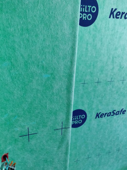 Grönt tätskikt i badrum med utskurna kryss för bubblor, redo för lagning med skarvremsa.
