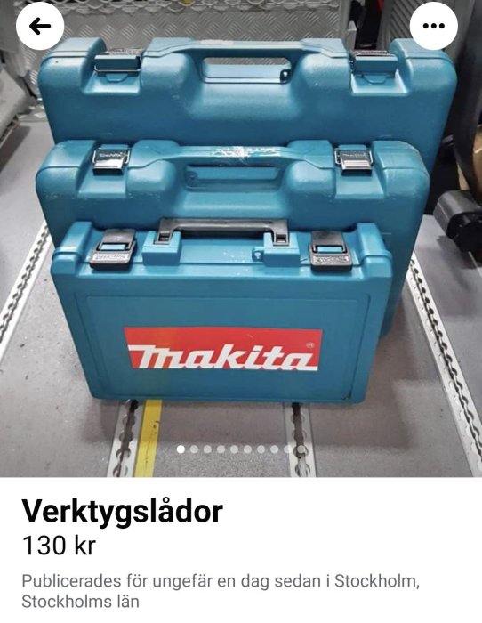 Staplad Makita verktygslådor i blå plast på ett metallgolv.