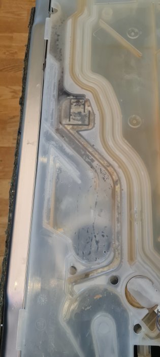 Rengjord plasttank från diskmaskin med synliga avlagringar och igensatt kanal.