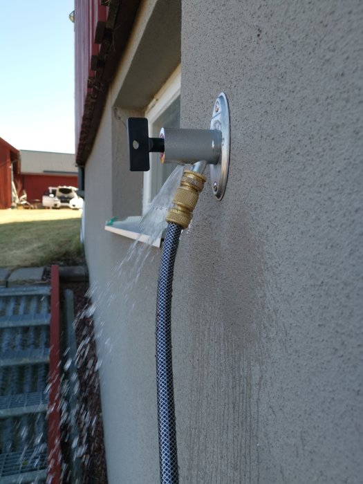 Vatten läcker från slangen kopplad till en utekran på en husvägg medan kranen är öppen.
