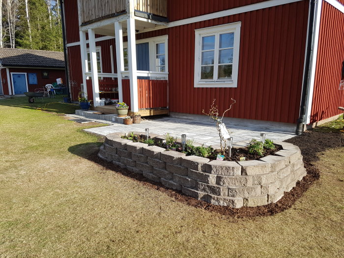 Nybyggd rabatt i mursten framför ett rött hus med stensatt gångväg.