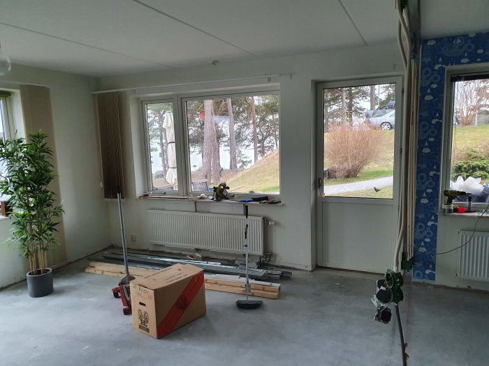 Tomt rum under renovering med verktyg, byggmaterial, och utsikt genom fönster.