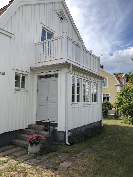 Ett vitt hus med befintlig, smal trappa av blocksteg och svart takpapp nära entrén, inför en renovering.