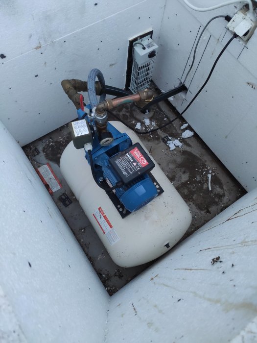 En vattenpump och hydrofortank i en brunn med synliga ledningar och en sprängd säkring.