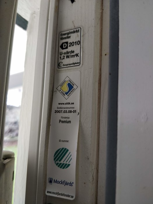 Etiketter på en altandörrkarm som visar energimärkning och tillverkarinformation.
