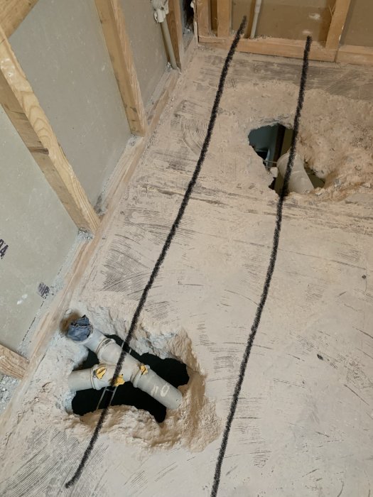 Lattialevy, jossa on kaksi isoa reikää putkien läpivientiä varten. Reikien reunat ovat karkeat, ja lattian alla näkyy putkia kiinteään liitokseen.