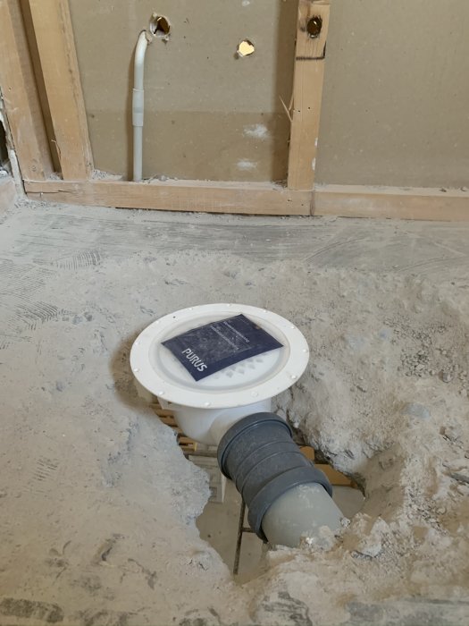 Suihkun lattiakaivon asennus keskeneräisen kylpyhuoneremontin aikana, näkyvissä on viemäriputkia ja avonainen betonilattia.
