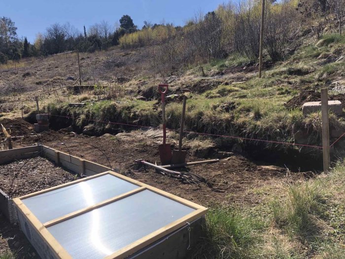 Pågående förberedelser för att bygga en stödmur med synligt berg, markerade nivåer och förarbeten, inklusive verktyg och byggmaterial.