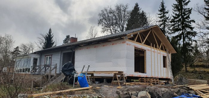 Delvis färdigställt hus med vindpapp, byggnadsställning och isoleringsmaterial runt omkring.