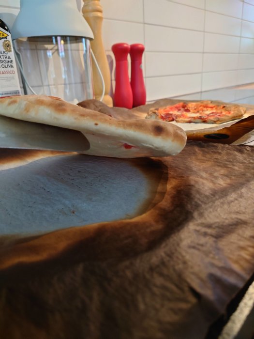 Nybakade hemmagjorda pizzor på en träskärbräda med bakplåtspapper, kryddkvarnar i bakgrunden.