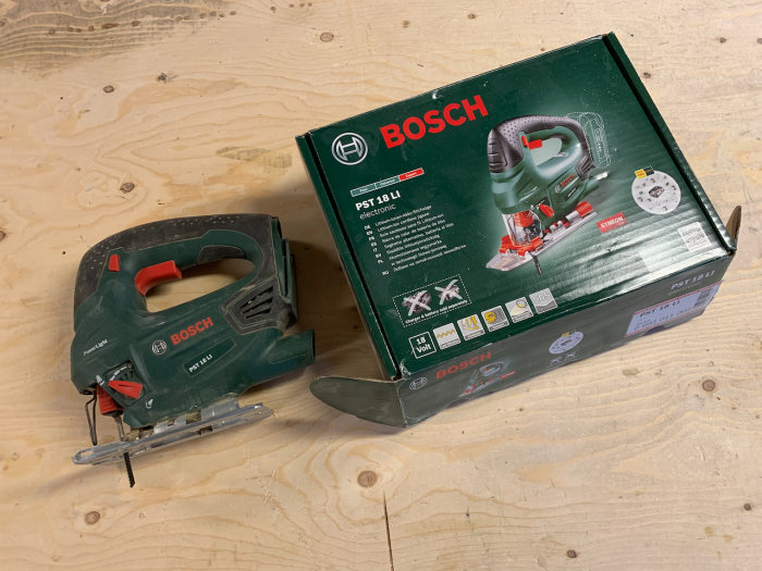 Bosch sticksåg PST 18 LI bredvid sin originalkartong på ett träbord.