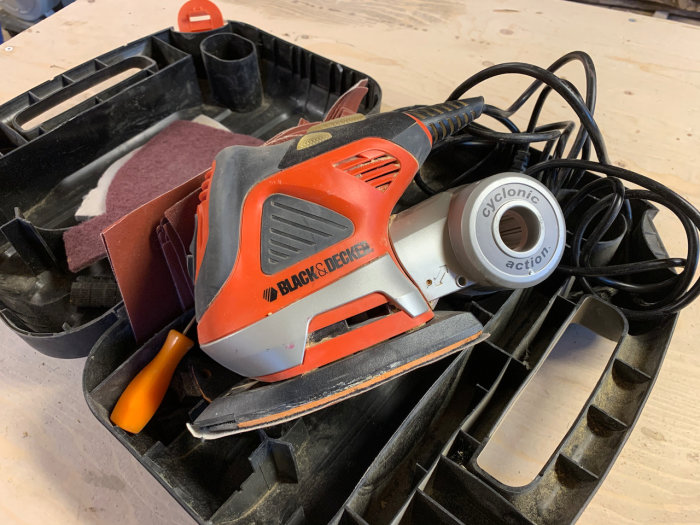 Använd Black & Decker Multislip i öppen svart plastväska med sladd och slipdynor.