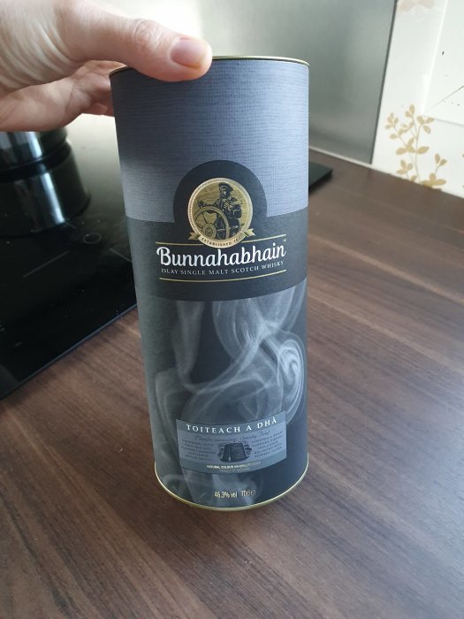 En hand håller en flaska Bunnahabhain Islay Single Malt Scotch Whisky i en cylinderformad förpackning.