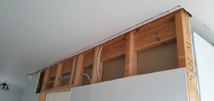 Öppnad vägg som visar träbjälklag och rörinstallationer, vilket illustrerar byggstrukturen för renovering.