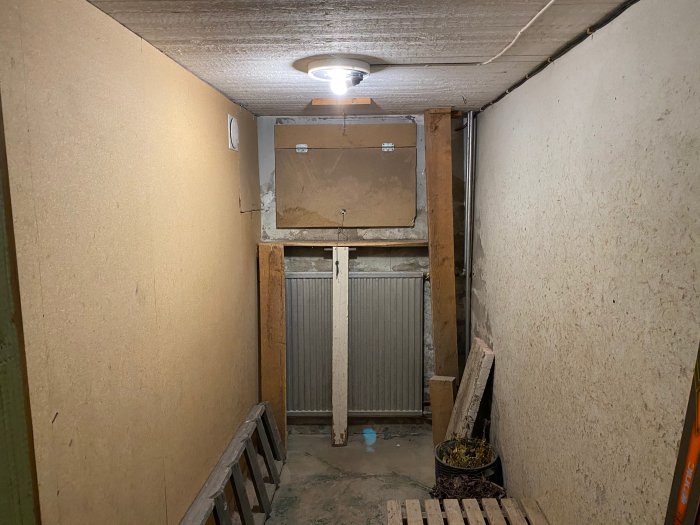 Ett källarförråd med bruna väggar, ett vedinsläpp och en radiator, som planeras att omvandlas till skidrum.