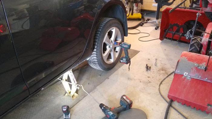 Bil upplyft med domkraft och sommardäck, Bosch-verktyg och bultar på garagegolv.