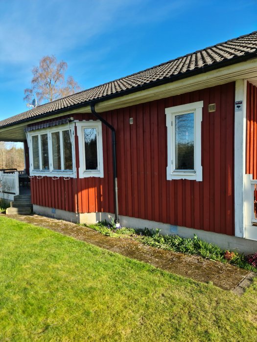 Rödfärgat trähus med vita fönster och svart tak, i behov av underhållsmålning.