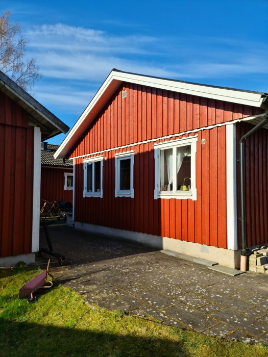 Ett rött trähus med vita fönsterkarmar och blå himmel i bakgrunden, fasad i behov av renovering.