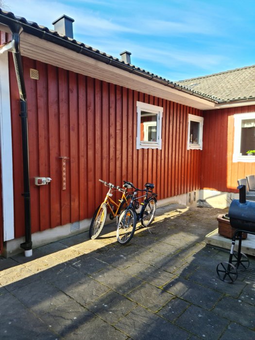 Rödfärgad träfasad på ett hus med vitmålade fönster och en dörr, cyklar lutade mot väggen.