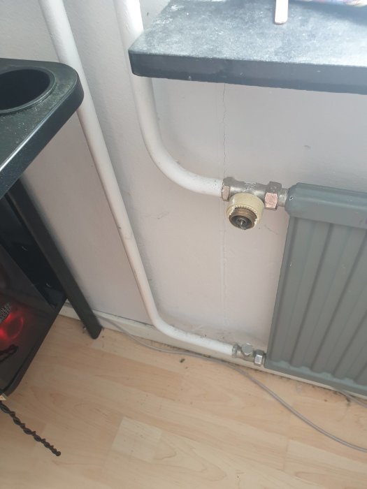 Radiator utan värme med synliga rör och termostat på en vägg nära ett bord och golv.