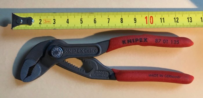 En liten Knipex Cobra vattenpumpstång bredvid ett måttband på en ljus yta.