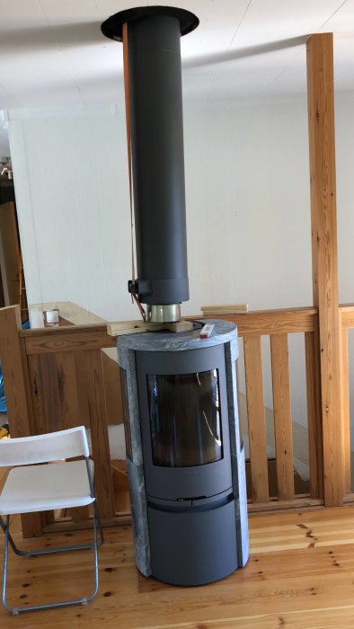 Kamin med hissad skorsten genom taket i ett träinrett rum under renovering.