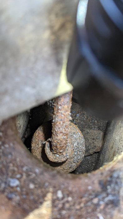 Rostig metallventil utan lock i schakt under marksten, omgiven av jord och grus.