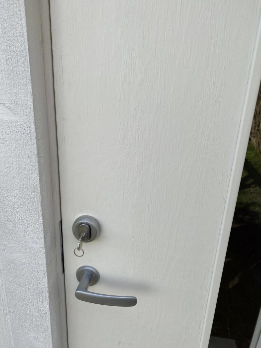 Vitmålad dörr med dörrhandtag och nyckel i låscylindern, fråga om försegling mot fukt.