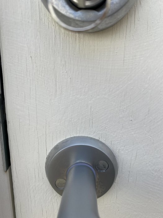 Närbild av en vitmålad dörr med en dörrhandtag och metallisk rosett, tecken på fukt eller åldring syns på ytan.