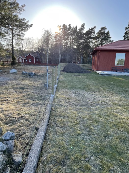 Pågående staketbygge som anpassats efter en sluttande tomt med stolpar längs med en snörelinje vid solnedgången.