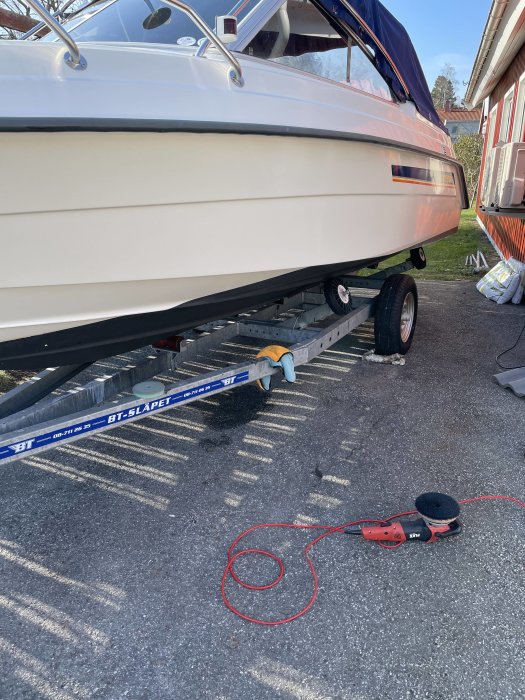 Motorbåt på trailer redo för sjösättning med polermaskin och förlängningssladd på marken.