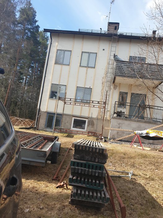 Byggmaterial och ställningsdelar framför hus under renovering med uppsatt ställning på ena sidan.