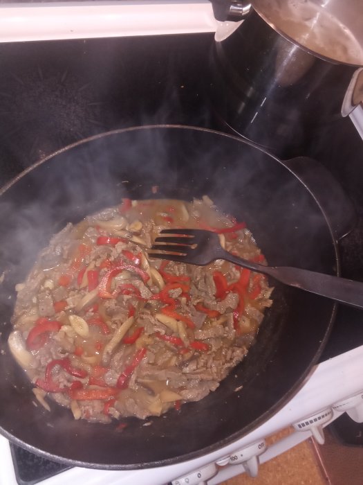 Stekpanna med lövbiff, paprika och lök, buljong och grädde, nästan färdigkokt pasta vid sidan.