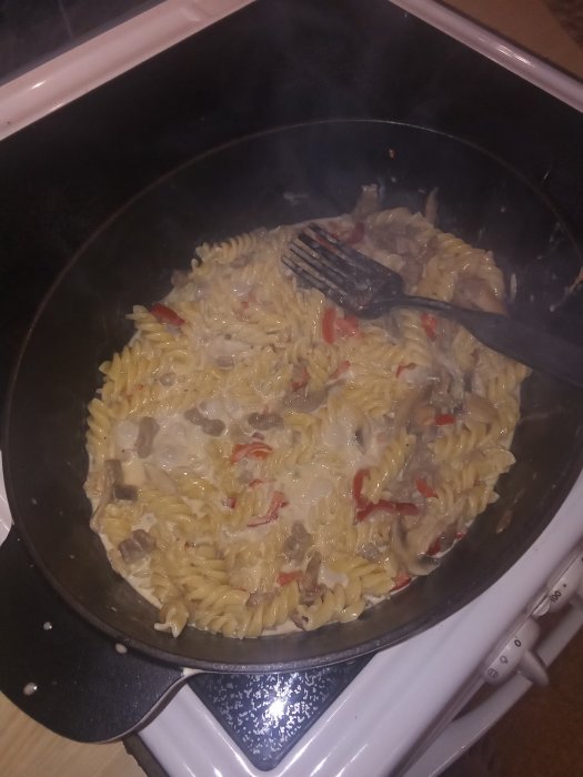 Pasta med lövbiff, paprika och lök i gräddig sås, omrörd i en stekpanna på en spis.