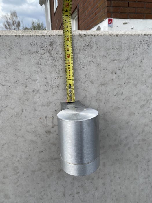 Måttband visar 15,5 cm från toppen av en stödmur till toppen av en utomhuslampa monterad på muren.