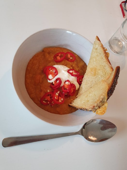 Skål med tjock sötpotatis-linssoppa, gräddfil, chili, varm macka på sidan.