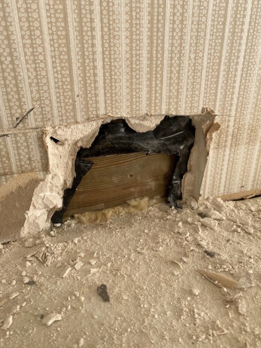 Skadad vägg med en delvis riven gipsskiva visar trä och isolering under.
