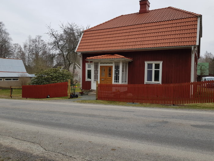 Rödmålat trähus med nygrundade röda staketstolpar framtill, jämnt gräs och en spjälad grind.