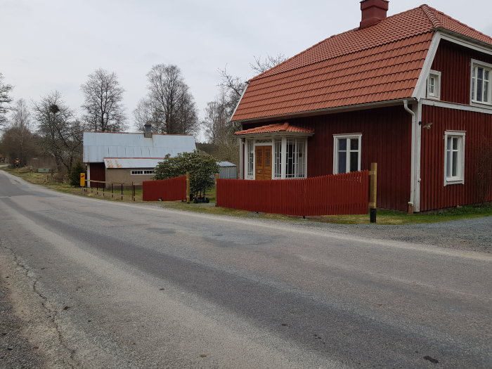 Rödmålat trähus med tegelröd takpannor och rött staket längs en grusväg.