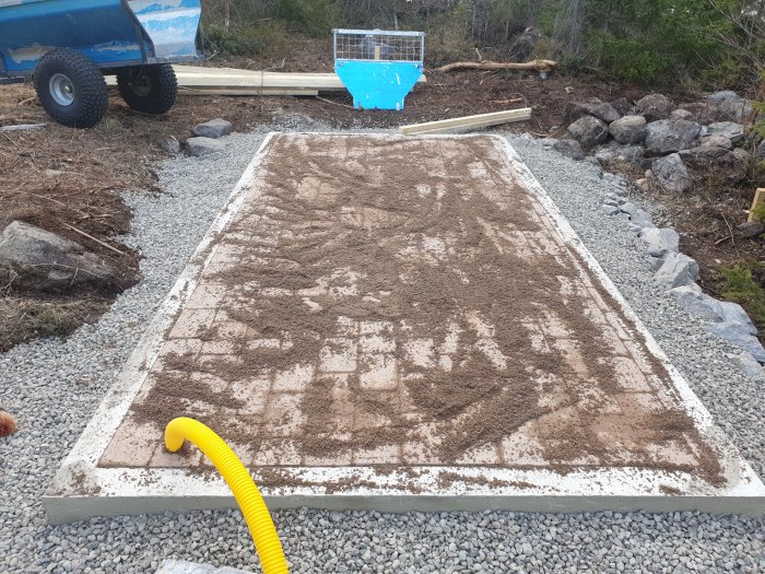 Stenplattor med utströdd fogsand och en gul trädgårdsslang ligger på ett pågående utomhus byggprojekt.