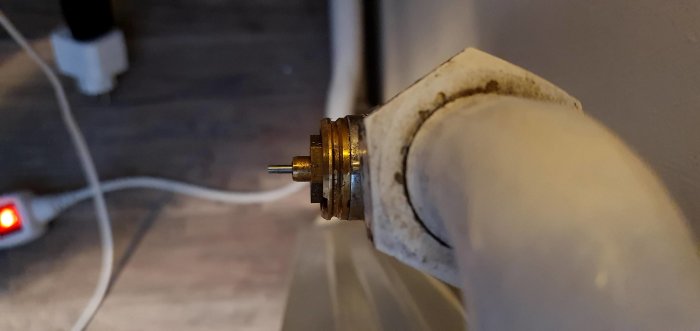 Närbild på ett gammalt vitmålat radiatorrör med en kopplingsdetalj mot väggen.