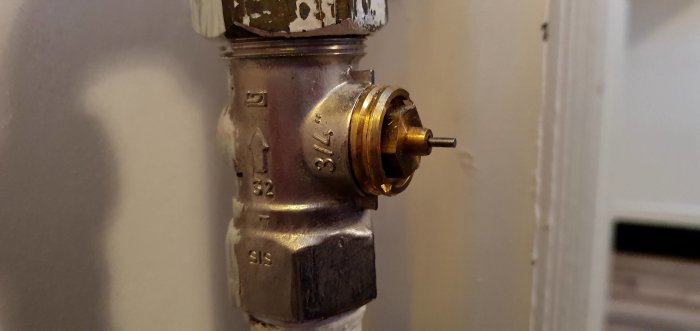 Närbild på en radiatorventil utan reglage monterad på en vit vägg.