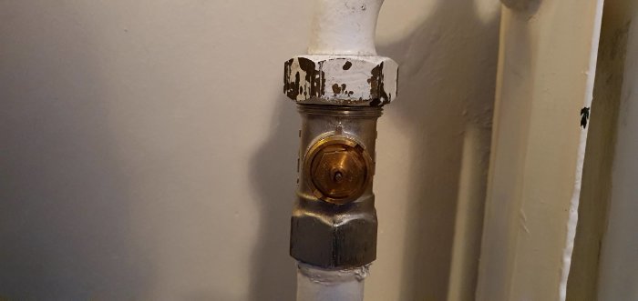 Närbild på en äldre vitmålad radiator med en mässingventil och flagande färg.