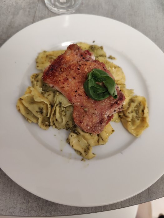 Kycklinglårfile med kryddig skorpa serverad på pestopasta, toppad med ett basilikablad.