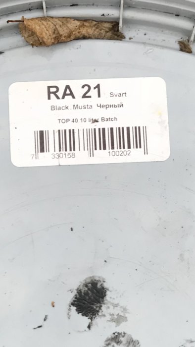 Etikett på en färgburk med texten "RA 21 Svart" och streckkod, med ett torrt löv ovanför.