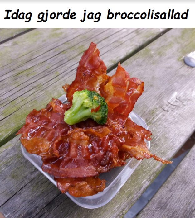 En skål med broccolisallad toppad med krispigt bacon på ett träbord.