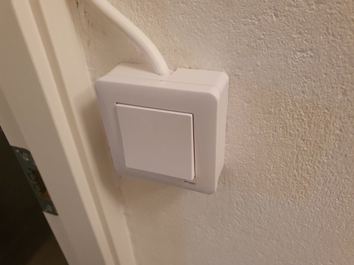 Vit strömbrytare på vägg bredvid vit kabel i en källaretoalett.